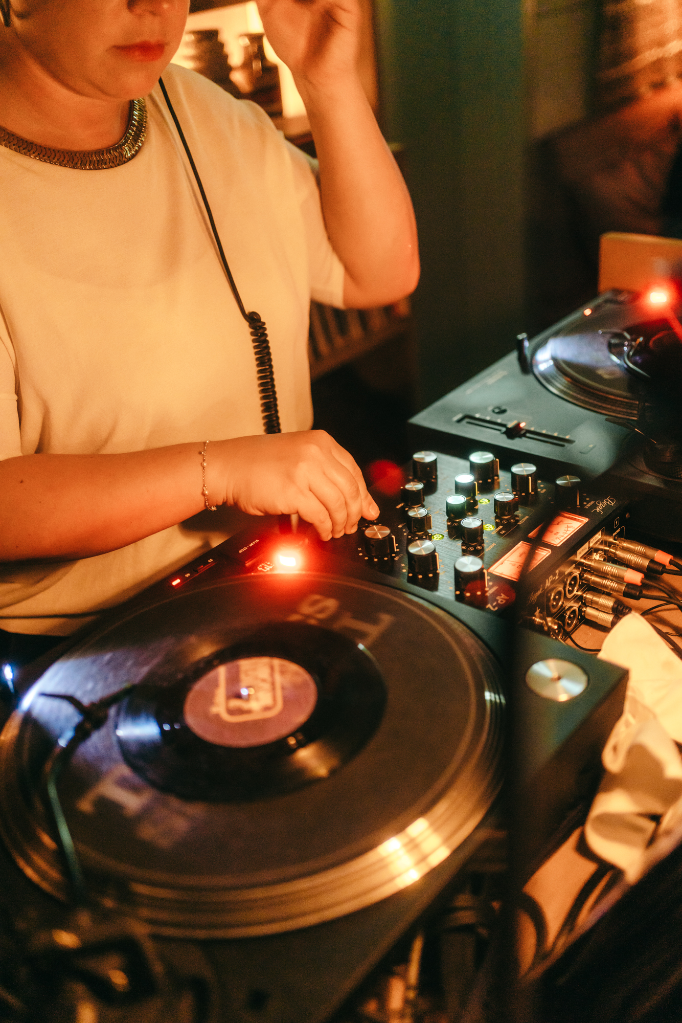 Close up of a DJ playing music inside the Shoreditch-based Seed Library hotel bar at a night party with warm lights.